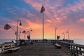 A shot of a long brown wooden pier with American flag flying on curved light posts with people fishing on the edge of the pier