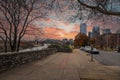 A shot of a long sidewalk with red brick with gorgeous autumn trees and parked cars along the street with powerful clouds