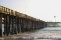 A shot of a long winding brown wooden pier at the beach with silky brown sand and vast blue ocean water Royalty Free Stock Photo