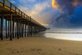 A shot of a long winding brown wooden pier at the beach with silky brown sand and vast blue ocean water Royalty Free Stock Photo