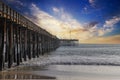 A shot of a long winding brown wooden pier at the beach with silky brown sand and vast blue ocean water Royalty Free Stock Photo