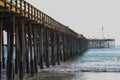 A shot of a long winding brown wooden pier at the beach with silky brown sand and vast blue ocean water Royalty Free Stock Photo