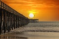 A shot of a long winding brown wooden pier at the beach with silky brown sand and vast blue ocean water Royalty Free Stock Photo