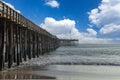 A shot of a long winding brown wooden pier at the beach with silky brown sand and vast blue ocean water Royalty Free Stock Photo