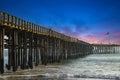 A shot of a long winding brown wooden pier at the beach with silky brown sand and vast blue ocean water Royalty Free Stock Photo