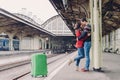 Shot of lovely boyfriend and girlfriend stand closely, embrace and kiss, wait for transport on railway station, being passengers, Royalty Free Stock Photo