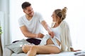 Lovely happy pregnant couple holding baby clothes on mothers belly and smiling on the sofa at home