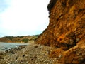 A shot of the lush green and red rock mountain landscape and the rocky beach and the ocean with waves crashing against the rock Royalty Free Stock Photo