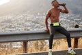 Shot of male runner drinks water after mountain running, feels thirsty, exercises outdoor early in morning, wears