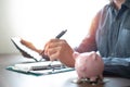 Shot of man's hand holding pen to write notebook with pink piggy bank for account save money.