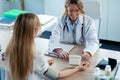 Mature beautiful female doctor measuring heart and blood pressure while taking care to young patient in the medical consultation Royalty Free Stock Photo