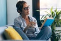 Mature beautiful woman reading a book sitting on couch at home Royalty Free Stock Photo