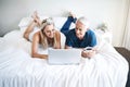 They have no plans to leave the house today. Shot of a mature couple using a laptop while relaxing on their bed at home. Royalty Free Stock Photo