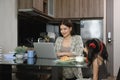 Shot of mother working with laptop with cute little daughter eating cookies at kitchen table Royalty Free Stock Photo