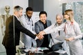 Shot of multiethnic medical team, doctors, scientists, lab researchers stacking hands together, having meeting in modern