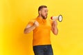 Shot of one bearded man holding megaphone and shouting over yellow background