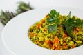 Shot of a a plate of Couscous with vegetables on a white table decorated with green plants