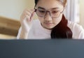 Shot of pleased beautiful Asian eyeglasses girl working with laptop while sitting at home
