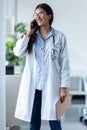 Pretty female doctor talking on mobile phone while standing in medical consultation Royalty Free Stock Photo