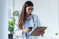 Pretty female doctor using her mobile phone while reviewing medical reports in medical consultation Royalty Free Stock Photo