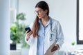 Pretty female doctor using her mobile phone while standing in medical consultation Royalty Free Stock Photo