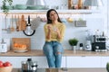 Pretty happy young woman eating yogurt while smiling thinking on her things sitting on the kitchen at home Royalty Free Stock Photo