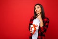 Shot of pretty positive young thoughtful brunette female person isolated over red background wall wearing white casual t Royalty Free Stock Photo