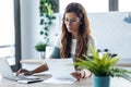 Pretty young business woman working with computer while consulting some invoices and documents in the kitchen at home Royalty Free Stock Photo