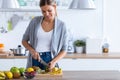 Pretty young woman cutting kiwi for preparing detox beverage in the kitchen at home