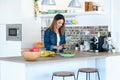 Pretty young woman cutting kiwi for preparing detox beverage in the kitchen at home Royalty Free Stock Photo