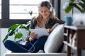 Pretty young woman listening to music with headphones and her digital tablet while sitting on sofa at home Royalty Free Stock Photo