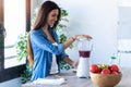 Pretty young woman mixing fruit in blender for fresh breakfast in the kitchen at home