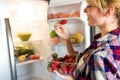 Pretty young woman picking strawberries of fridge in the kitchen. Royalty Free Stock Photo