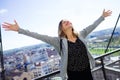 Pretty young woman with raised arms to the sky enjoying the time at modern rooftop of high-rise building. Royalty Free Stock Photo