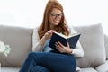 Pretty young woman reading a book while sitting on the sofa at home. Royalty Free Stock Photo