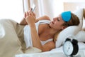 Pretty young woman sending text message with her smartphone after wake up in the bedroom at home. Royalty Free Stock Photo