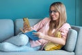 Pretty young woman using her mobile phone while reading a book on sofa at home Royalty Free Stock Photo