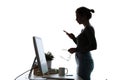 Pretty young woman using her mobile phone while standing in front of computer over white background Royalty Free Stock Photo