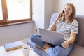 Shot of pretty young woman using her mobile phone while working with laptop sitting on comfortable couch at home Royalty Free Stock Photo