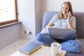 Shot of pretty young woman using her mobile phone while working with laptop sitting on comfortable couch at home Royalty Free Stock Photo