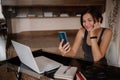 Shot of pretty young woman using her mobile phone while working with laptop sitting at home. Royalty Free Stock Photo