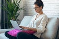 Pretty young woman working with her laptop while sitting on couch at home Royalty Free Stock Photo