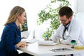 Pretty young woman talking with handsome young doctor about her health in the consultation. Royalty Free Stock Photo