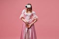 Shot of princess wearing dress and virtual reality glasses holding grapefruit over pink studio background. Escape from Royalty Free Stock Photo