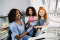 Shot of professional female african dentist and her two little patients, multiethnic shcoolgirls, sitting in dentistry