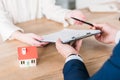 Shot of realtor giving pen and clipboard with loan agreement to customer near house model