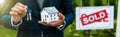 Shot of realtor holding carton house model and keys near board with sold letters