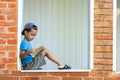 A serious little boy sits on the veranda near the old village house and reads book