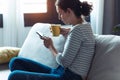 Serious young woman using her mobile phone while sitting on sofa in the living room at home Royalty Free Stock Photo