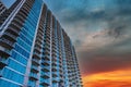 A shot of a skyscraper with rows of balconies with gray metal rails and glass windows with powerful clouds in the sky at sunset